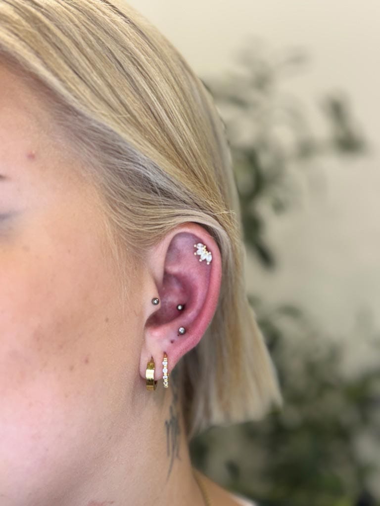 Nahaufnahme eines Ohrs mit mehreren Ohrringen; blondes Haar, neutrale Hintergrundfarbe.